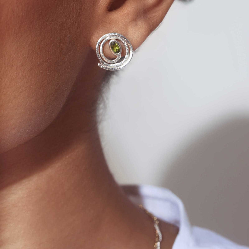 Model wearing silver hammered spiral earrings with peridot gemstones